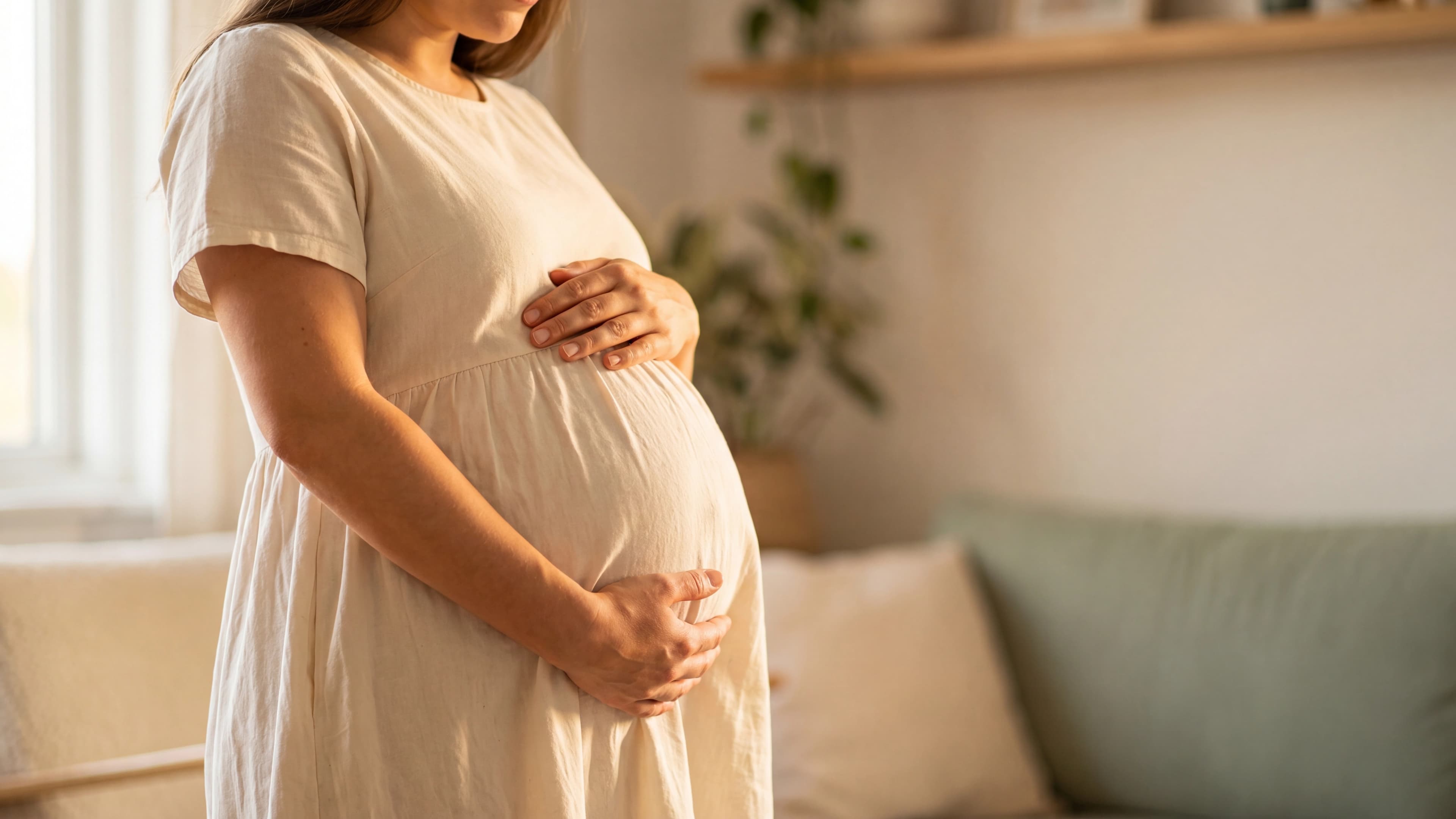 Mulher grávida segurando o ventre em sala iluminada por luz natural